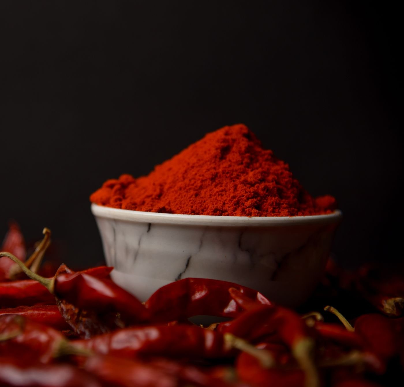 A bowl of red chilli powder with dried chillies